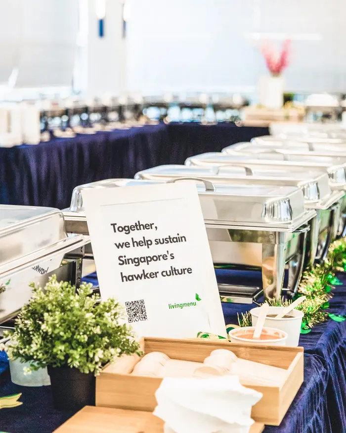 Buffet catering line at a company celebration with a sign about sustaining hawker culture