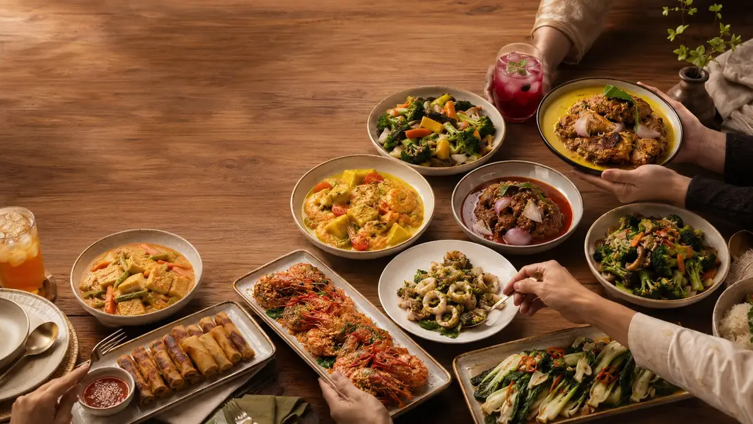 Hands reaching for a local catering spread of curry, sambal prawns, spring rolls and stir-fried vegetables in Singapore